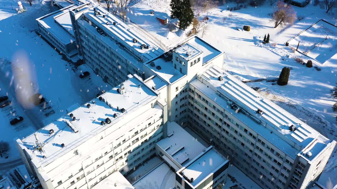 Sykehuskompleks dekket av snø, spesialisert innen helsevesen og medisin, sett fra luften på en solrik vinterdag.