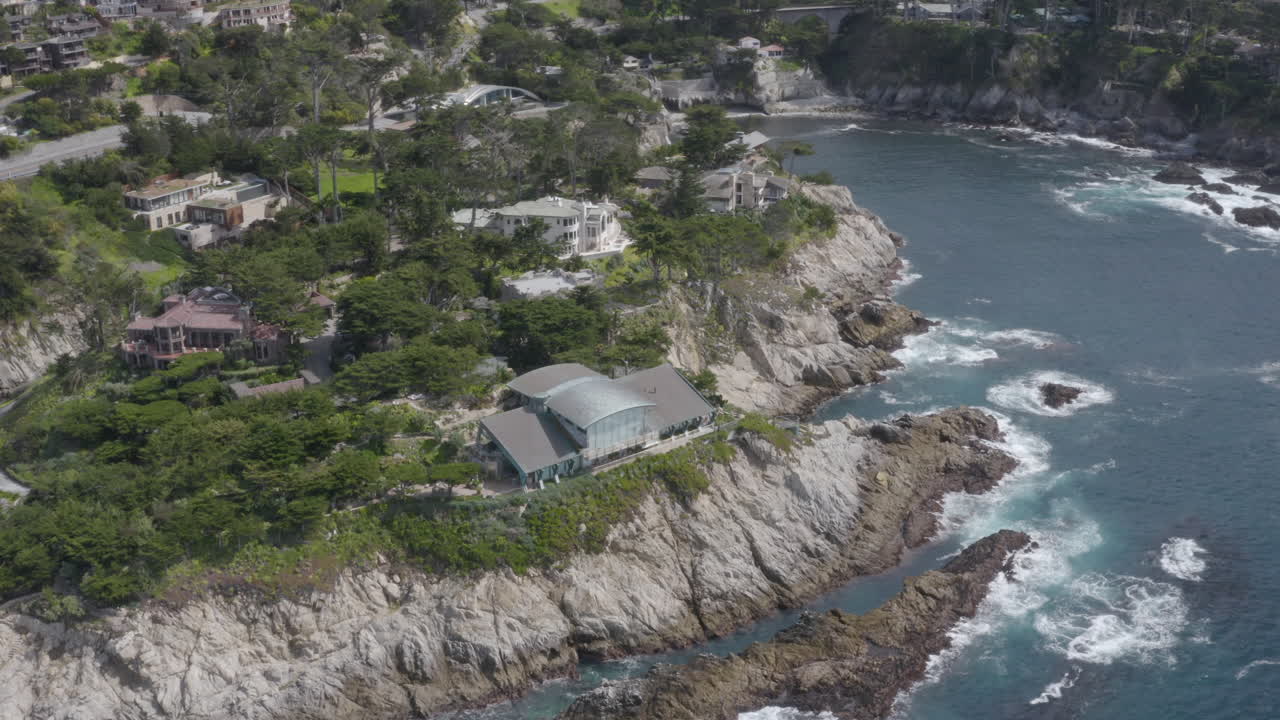4K aerial view of cliff side homes and cove with PCH in the background in the Carmel Highlands California.