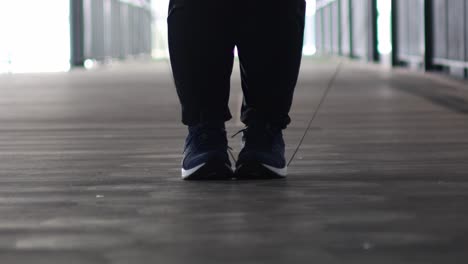 Close-up of feet performing jump rope exercise on a wooden walkway with rhythmic motion.