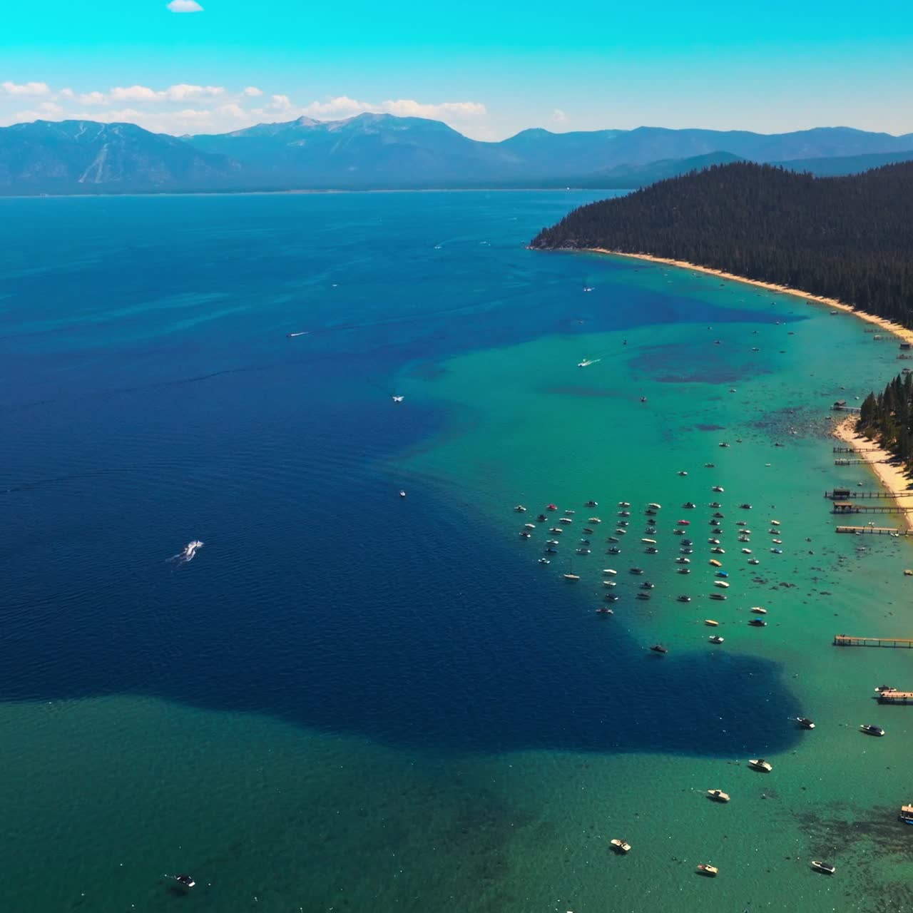Stunning turquoise scenery of Lake Tahoe with boats sailing on. Huge forest of pine trees covering the land. Top view