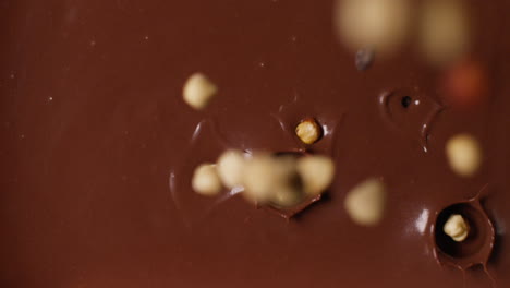 close up overhead shot of hazelnuts being dropped into melted chocolate sauce 1