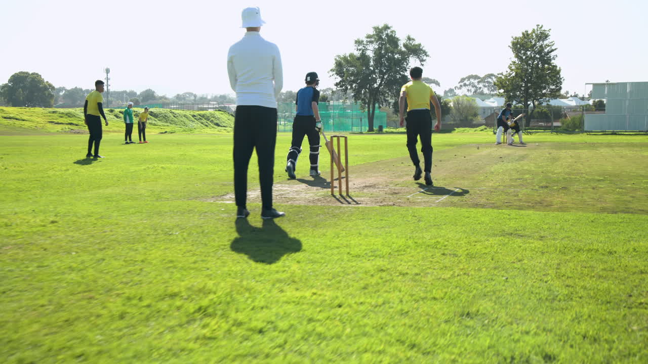 Umpire signaling during outdoor cricket match, players preparing on sunny field