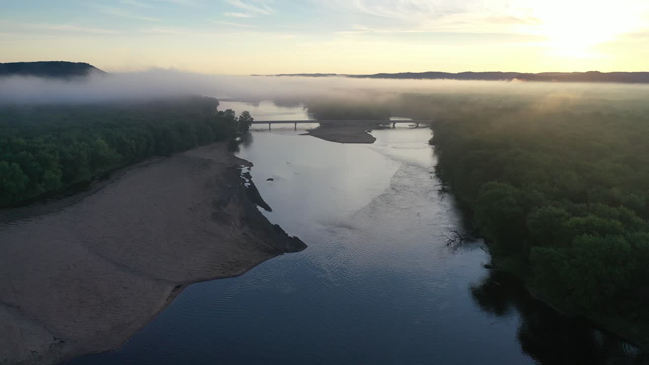 안개가 가득한 아침 강의 해가 뜨고 다리가 있습니다.