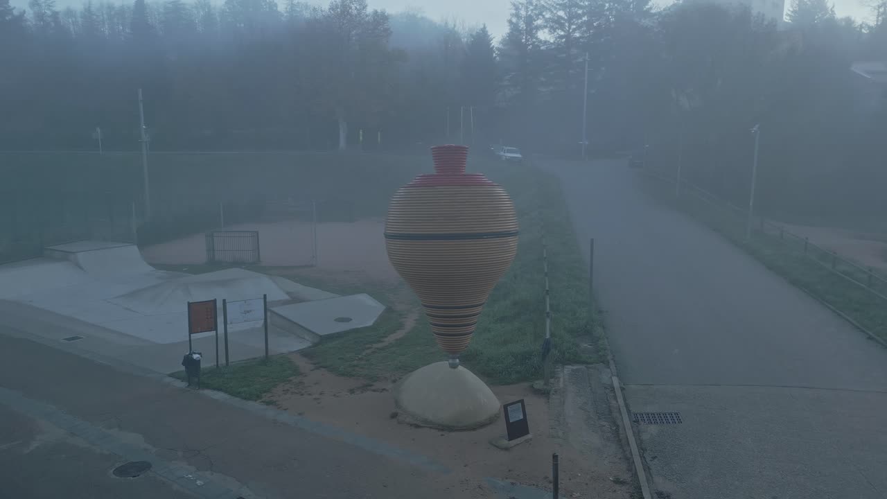 Fog slowly envelops the giant spinning top sculpture in sant hilari sacalm, spain, creating a mysterious and surreal atmosphere in a public park