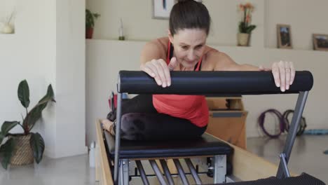 Fit-senior-caucasian-woman-stretching-on-reformer-in-pilates-studio,-unaltered,-in-slow-motion