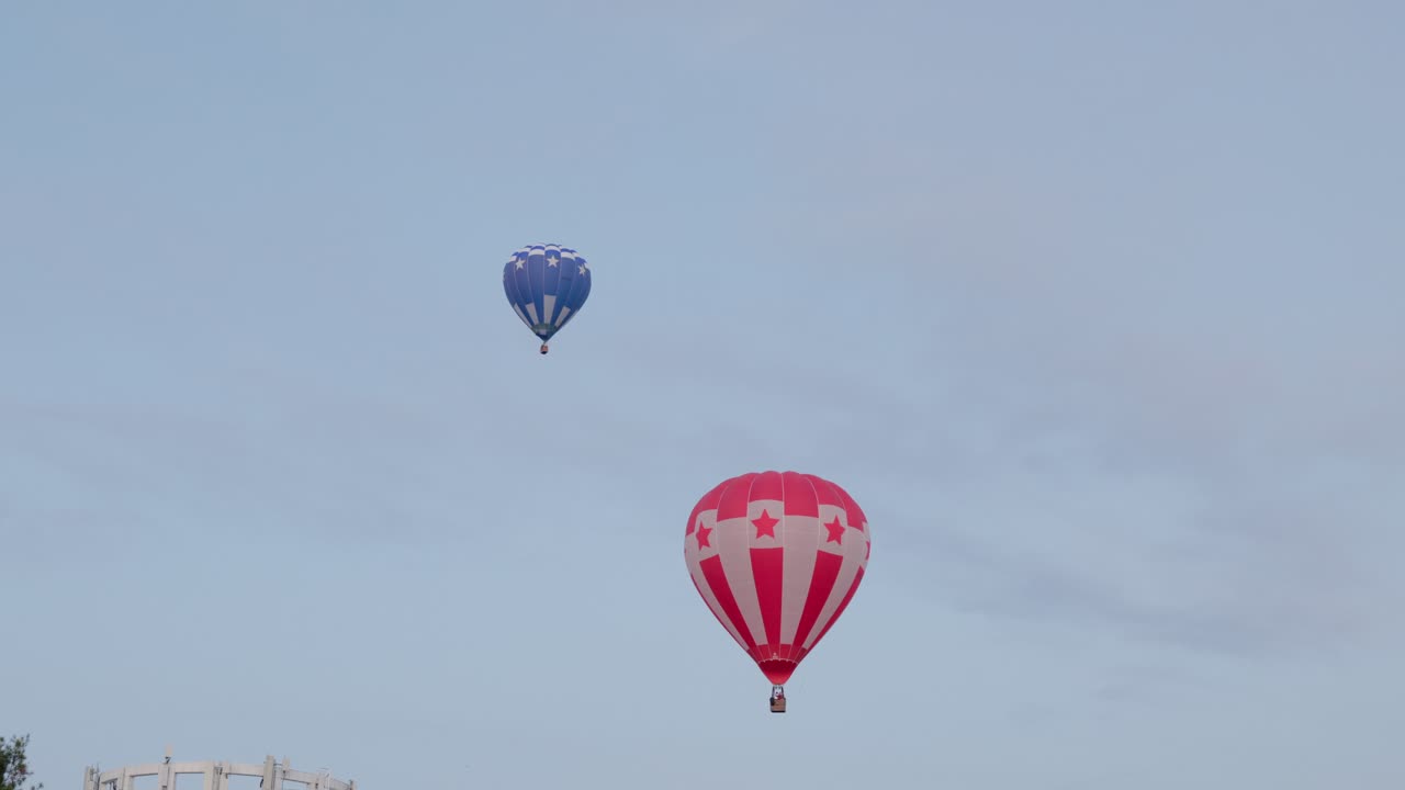 A pair of colorful hot air balloons drift across the sky at sunrise, creating a picturesque moment during the Canberra Balloon Spectacular.