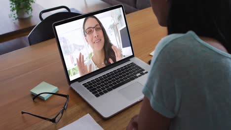 Mixed-race-businesswoman-sitting-at-desk-using-laptop-having-video-call-with-female-colleague