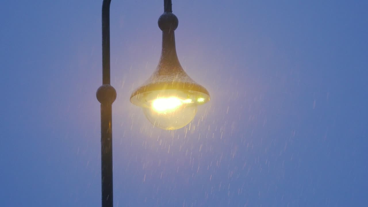 Snow falls by a light post