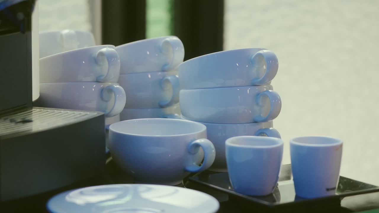 Blue ceramic cups stacked on tray next to coffee machine indoors