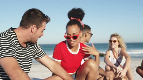 jóvenes amigos adultos sentados en una playa hablando 4k