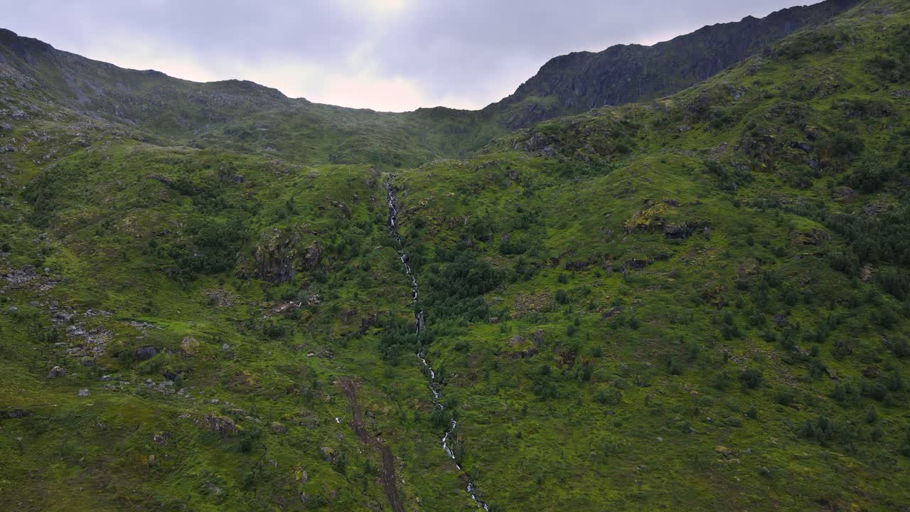 노르웨이의 풀이 무성한 산의 안장 가장자리 위로 흐르는 폭포의 공중 전망