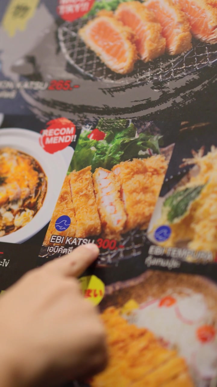 Lähikuva käsistä valitsemassa ruokia värikkäältä japanilaiselta ruokalistalta matalalla syväterävyydellä