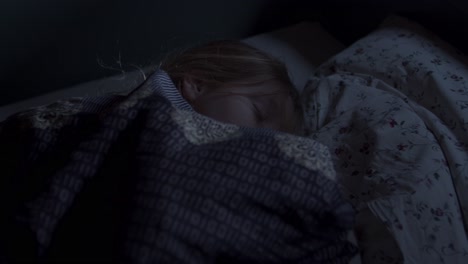 a little girl sleeps peacefully cuddled up in the covers in her bed