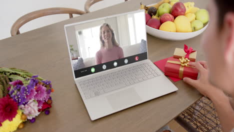 mujer caucásica sosteniendo un regalo rojo usando una computadora portátil con una mujer caucácea en la pantalla