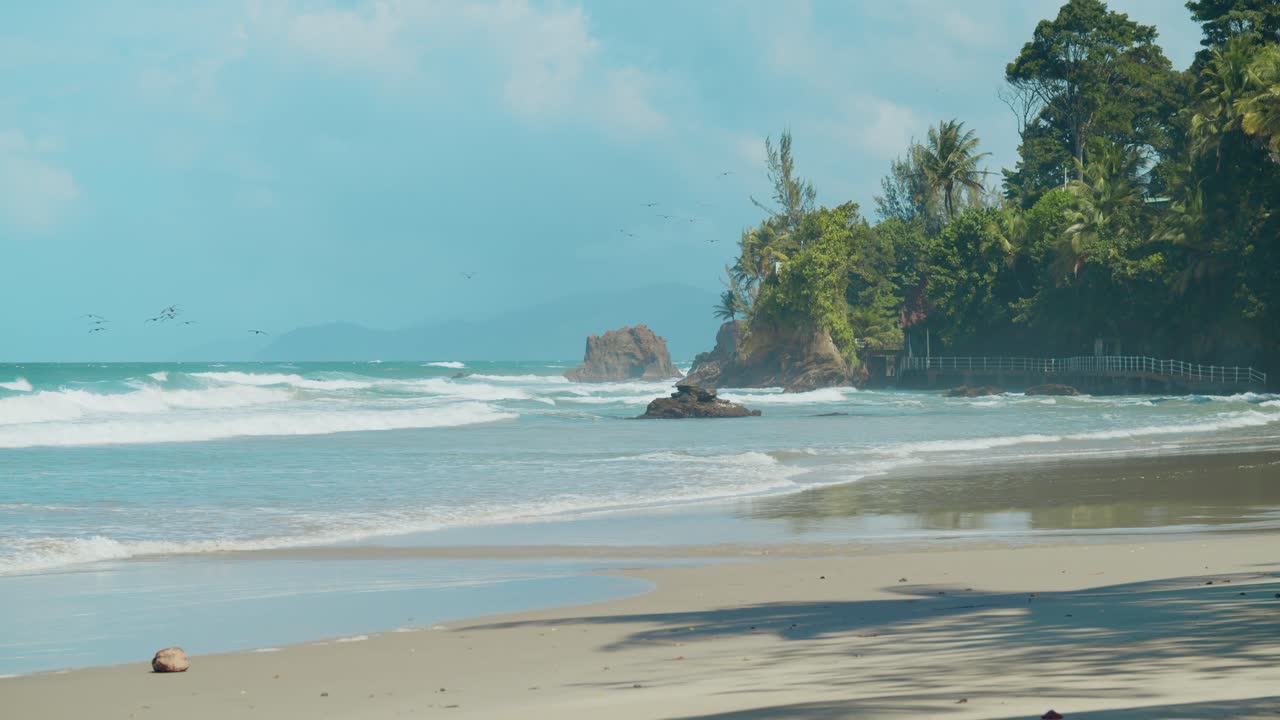 Pemandangan pantai tropis yang memukau dengan ombak bergelombang dan langit biru jernih membentang hingga cakrawala