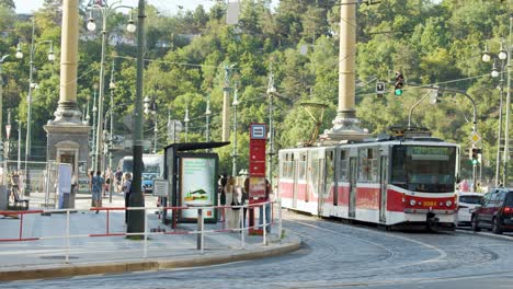 two cyclists pass a tram on a sunlit prague bridge; camera remains stationary