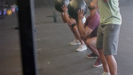 Diverse-male-group-fitness-class-training-at-gym-lifting-and-throwing-medicine-balls,-in-slow-motion