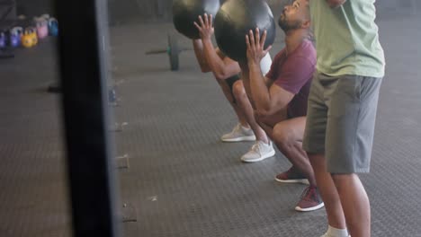 diverse male group fitness class training at gym lifting and throwing medicine balls, in slow motion