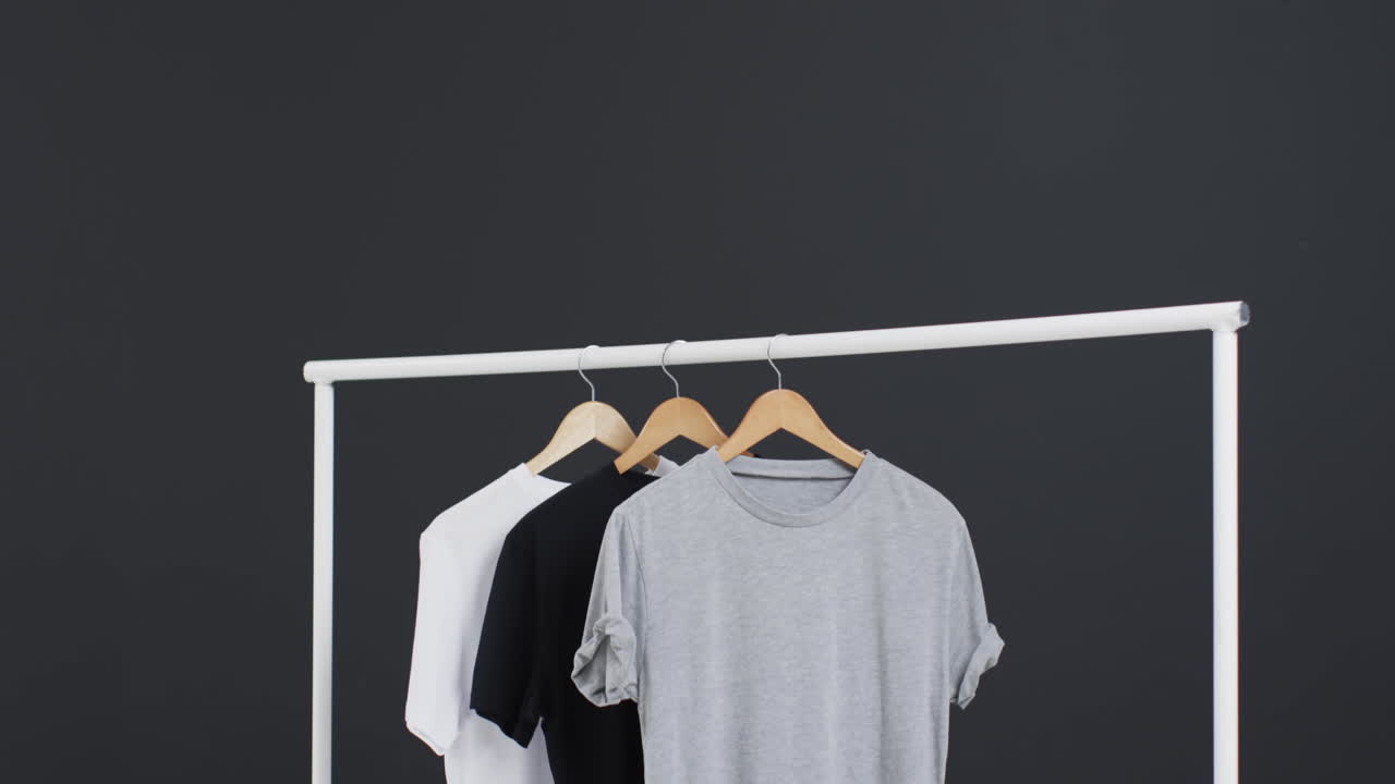 Video of three white, black and grey t shirts on hangers and copy space on black background