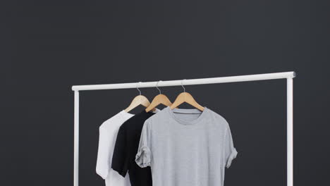 video de tres camisetas blancas, negras y grises en perchas y espacio de copia en fondo negro