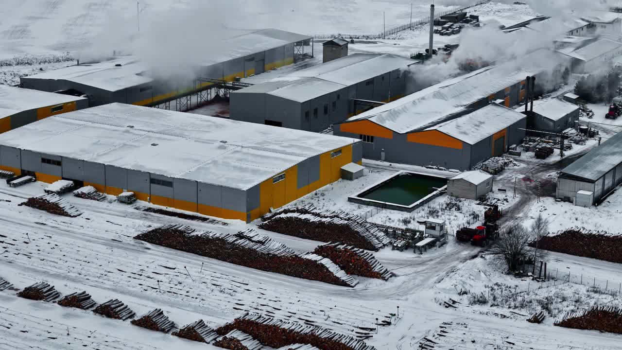 Large industrial warehouses with snow-covered roofs and steam rising in a winter landscape