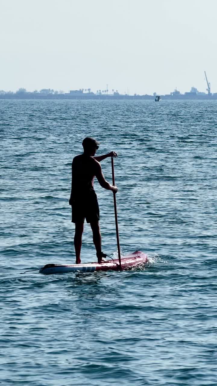 Paddle surfer gliding across calm ocean waters. Vertical