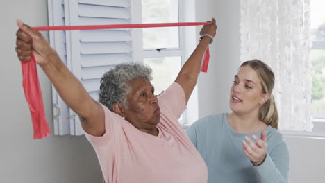 caucasian nurse with senior woman exercising with rubber band, copy space, slow motion