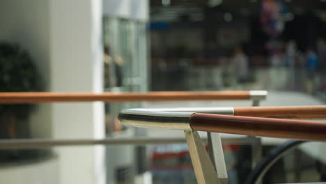 una escena dinámica del centro comercial capturada desde una perspectiva en primera persona con una cámara de mano, con un fondo borroso. el enfoque está en las elegantes barandillas de madera mientras un hombre y una mujer pasan