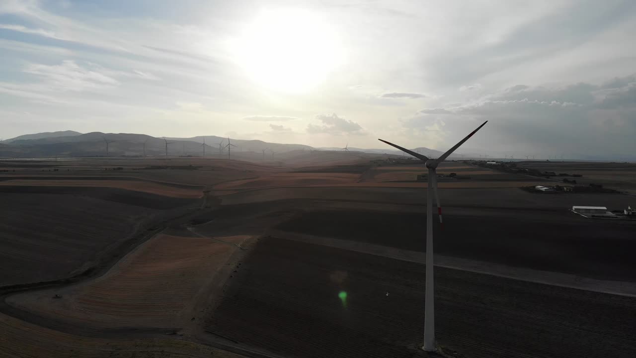 Drone flies around a solitare wind turbines during sunset on fields in Daunia- Puglia