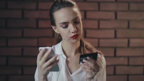 young woman using mobile phone and bank card for shopping online in brick studio