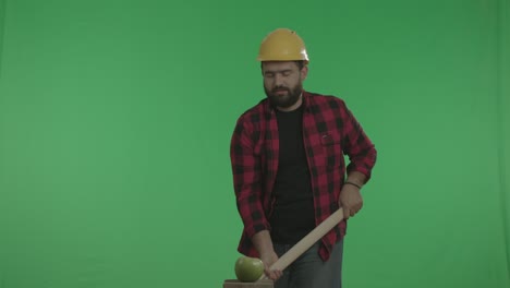 un trabajador industrial gracioso está destrozando una manzana con un martillo.
