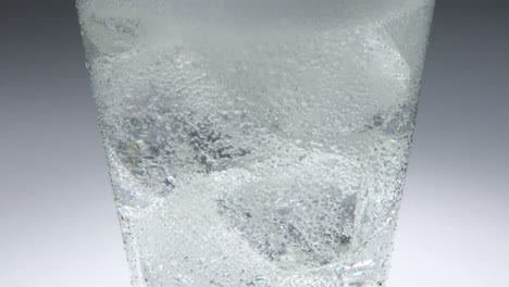 close up of ice in a glass into which a fizzy clear drink is slowly poured