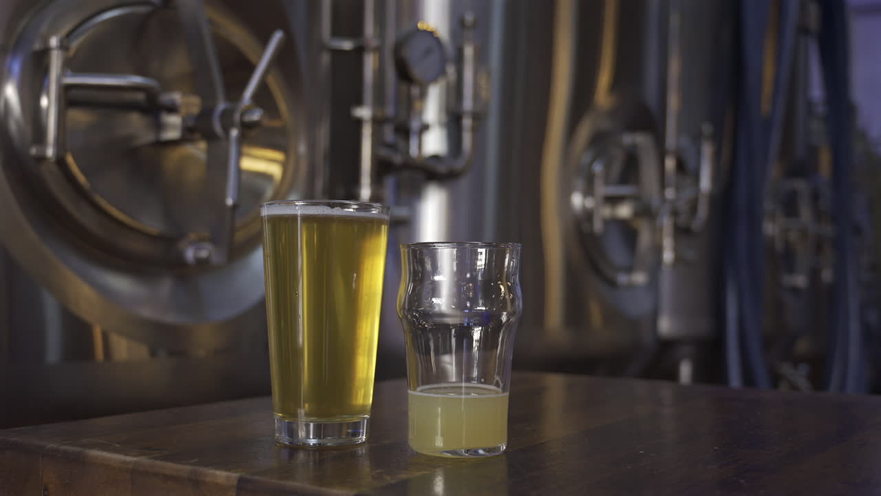 Close up of two beer glasses with stainless steel tanks on the background
