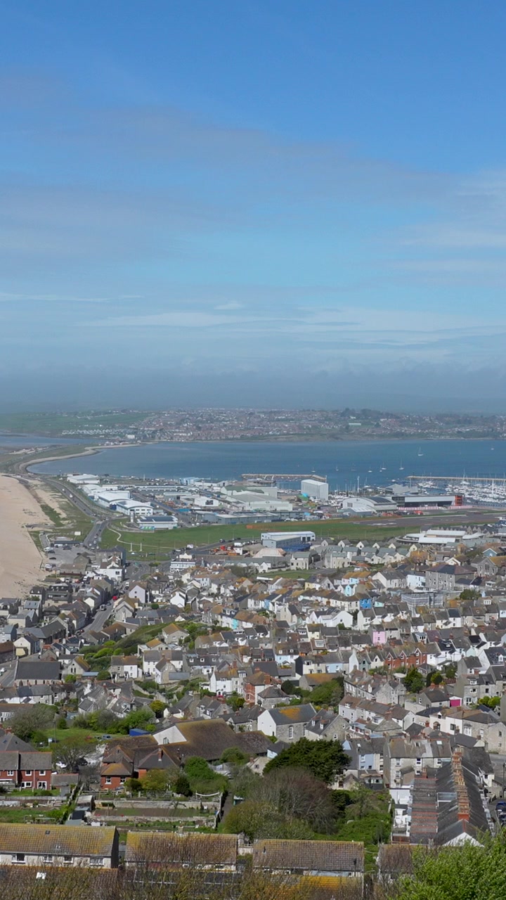 Eine filmische Aufnahme aus der Vogelperspektive mit Blick auf die dichte Bebauung und den Hafen von Weymouth und Portland, die die wunderschöne englische Küste und das blaue Meer zeigt