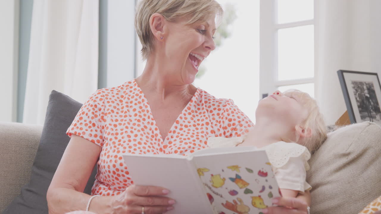 집에서 손녀와 함께 소파에 앉아서 책을 읽고 있는 할머니