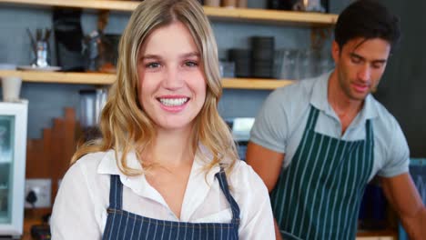 Smiling-waitress-in-front-of-colleague-working-in-background