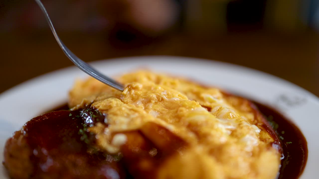 Close-up of fork lifting gooey cheese from omurice with demi-glace sauce, shallow depth, natural light