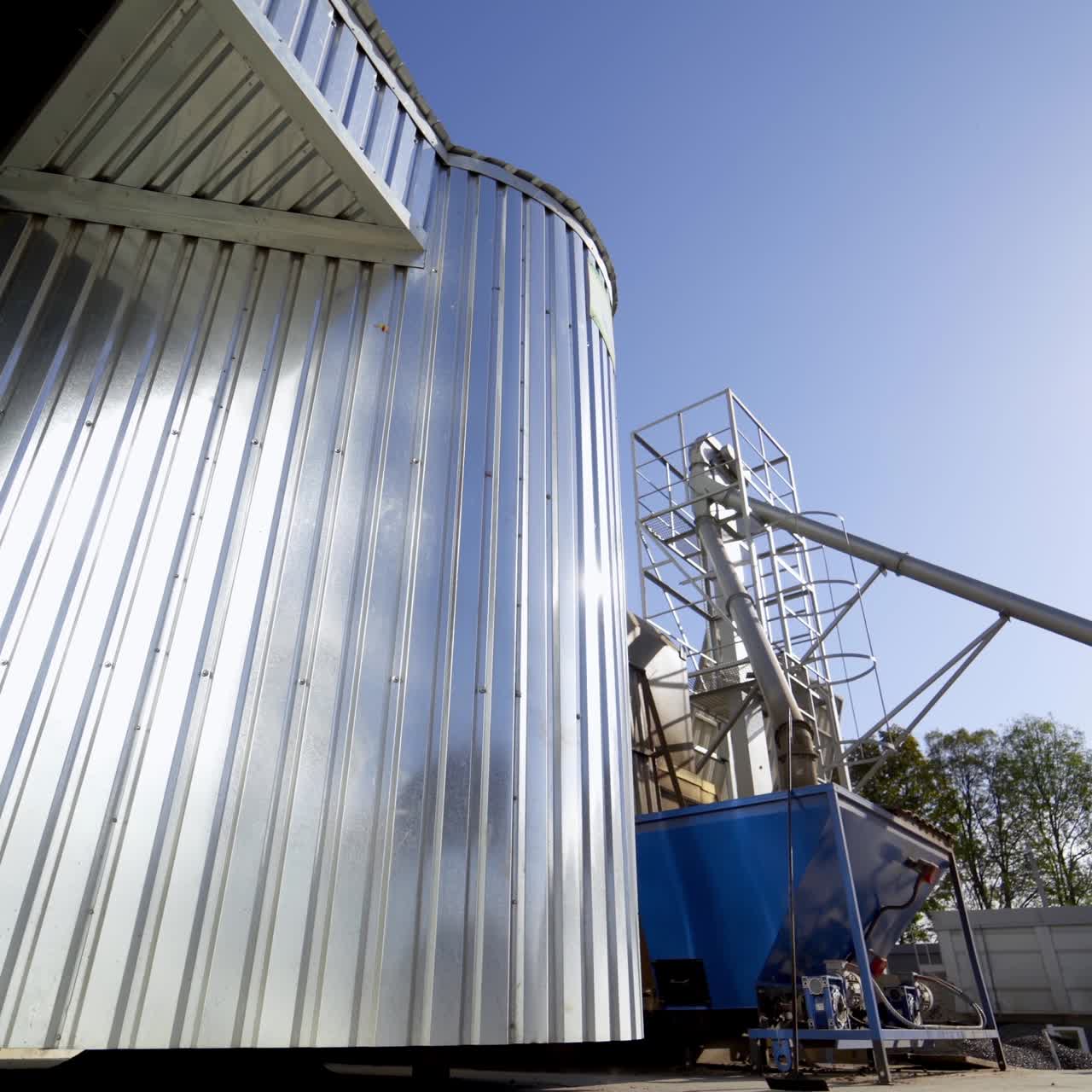 Metal granary at sunlight. Modern plant for processing agricultural harvest. Silver grain elevators in summer. Industrial complex for storing crop. Close-up.