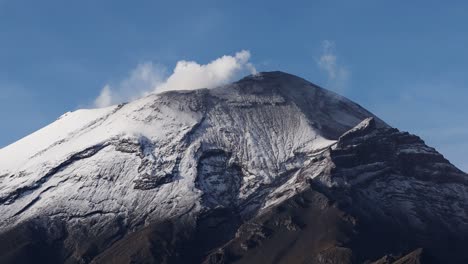 a detailed view of popocatépetl volcano, showing its snow-covered summit and wisps of smoke rising from its crater, against a clear blue sky.