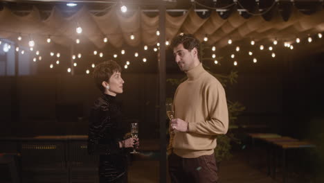 elegant woman and handsome man holding champagne glasses and talking to each other at new year's eve party