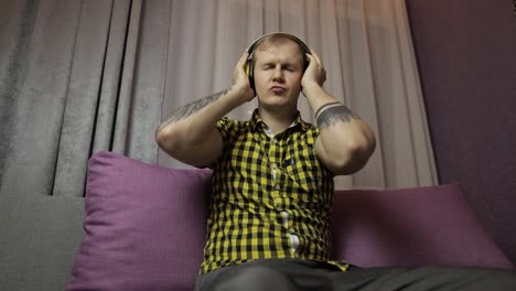 man sitting on the sofa listens music from wireless headphones and dances