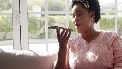 african american woman speaks into a phone, sunlight streams in at home