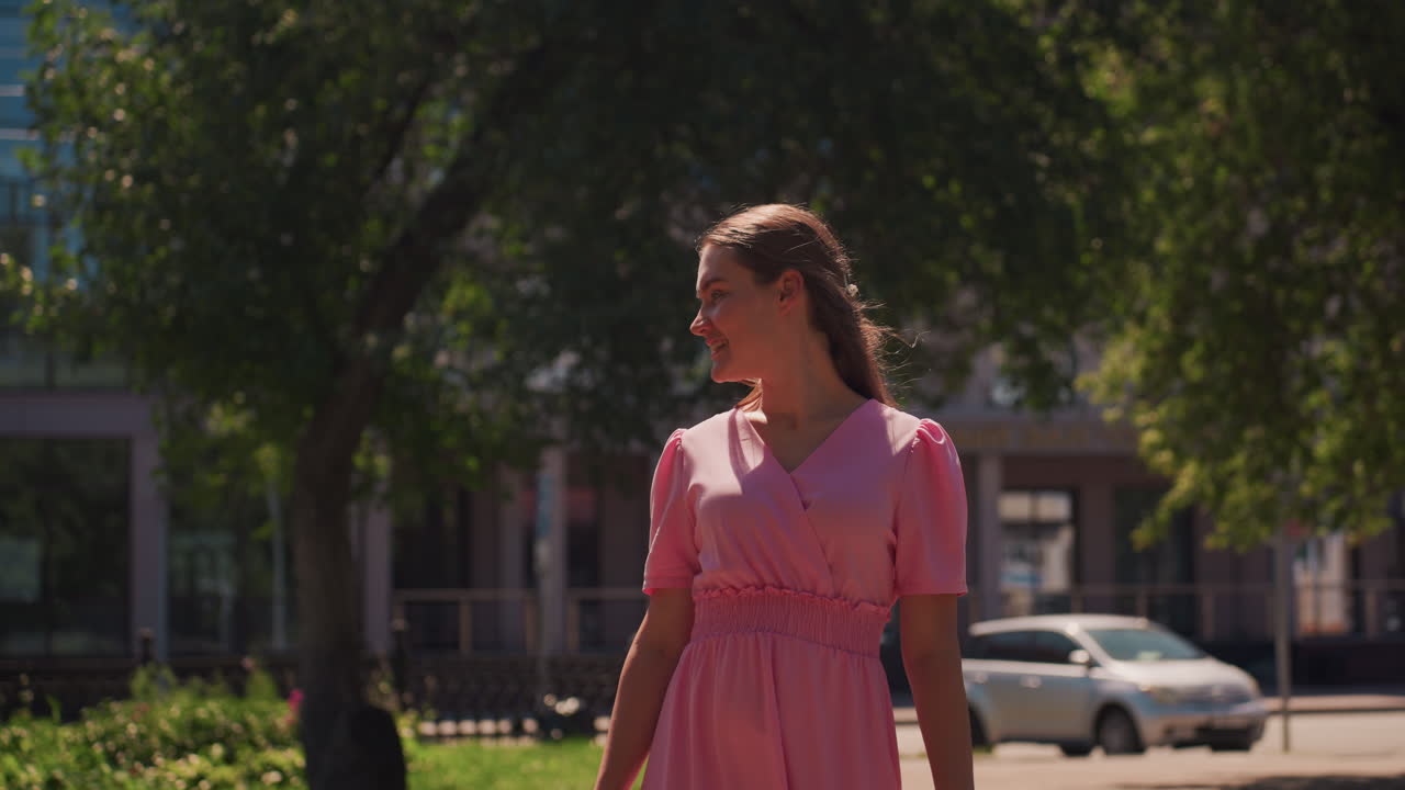 Mulher branca sorrindo em um parque ensolarado, vestido rosa esvoaçante, olhando para cima sob as árvores frondosas e a rua moderna, brisa suave e luz do dia quente, olhar alegre e sincero e risadas, cinematográfico e vibrante