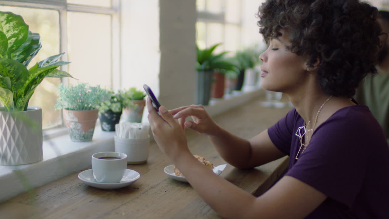 joven mujer afroamericana usando un teléfono inteligente en una cafetería navegando por mensajes en línea bebiendo café elegante mujer negra enviando mensajes de texto compartiendo estilo de vida en las redes sociales disfrutando del teléfono móvil