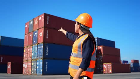 a warehouse worker in safety gear directing attention towards stacked shipping containers in a busy port environment under clear blue skies