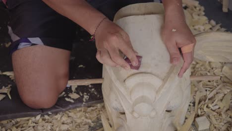 indonesian craftsman sanding a wooden piece of barong mask