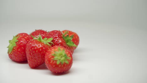 six red strawberries rotating on the table with pure white background - close up shot