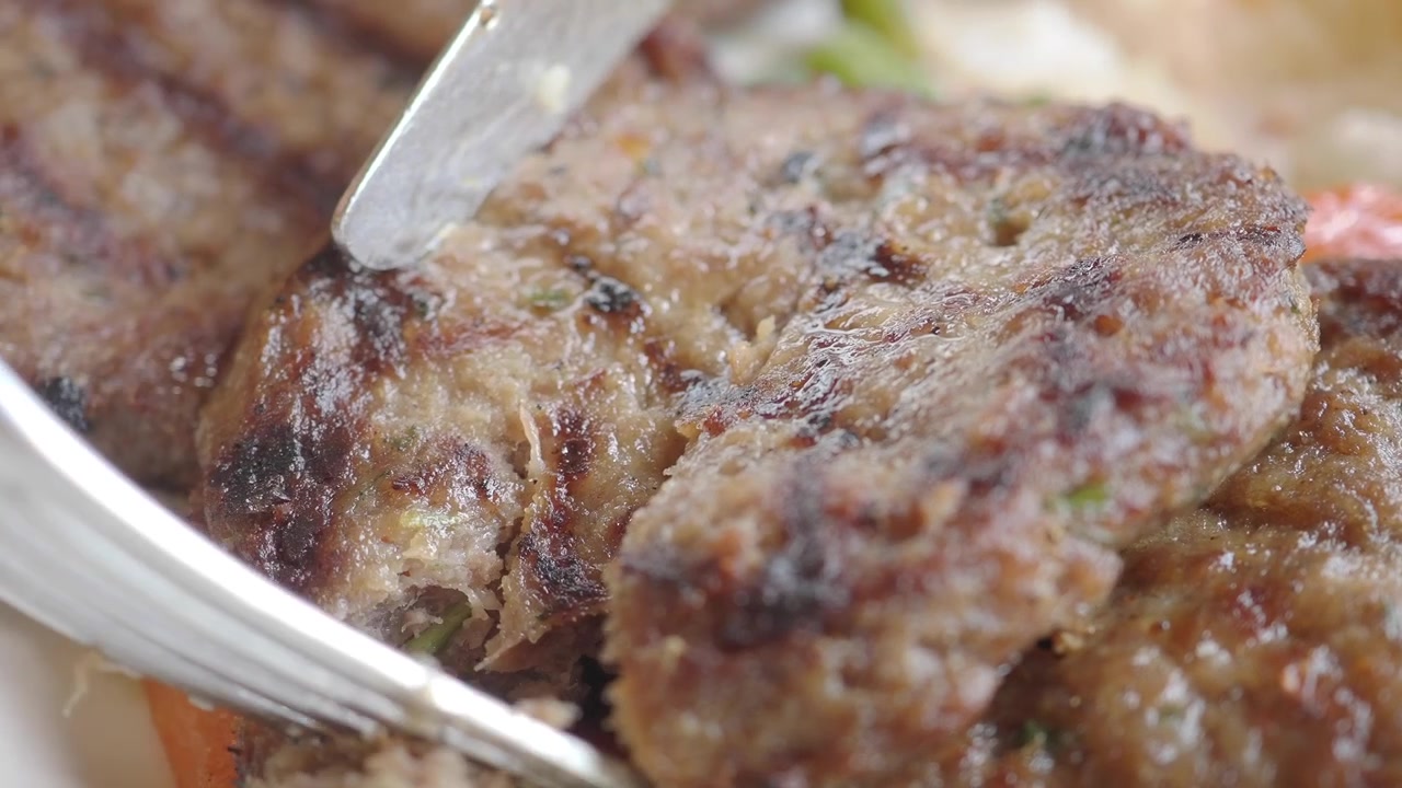 Primo piano del taglio di un hamburger di carne alla griglia con forchetta e coltello.