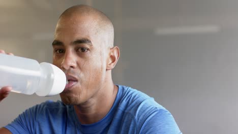 hombre biracial cansado descansando y bebiendo agua después del entrenamiento en el gimnasio, en cámara lenta
