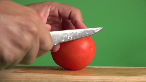 un cuchillo cortando horizontalmente un tomate sobre un fondo cromático